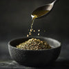 Olive oil pouring from spoon over za’atar spice blend in black ceramic bowl on dark background