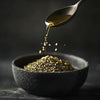 Olive oil pouring from spoon over za’atar spice blend in black ceramic bowl on dark background