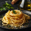 Golden pasta elegantly twirled on a matte black plate with olive oil drizzle, parmesan, and parsley garnish, styled with cinematic lighting and luxury editorial detail