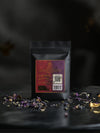 Back of Zhourat tea pouch showing ingredients, QR code, and steeping information with loose herbs around the base