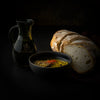 Sliced artisan bread with dipping oil infused with herbs and spices, next to a Mediterra olive oil bottle on a dark background.